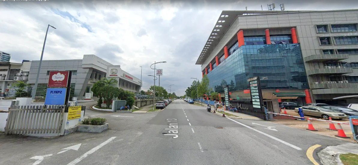 Exterior type: commercial building; features: glass curtain wall, red accent panels, multiple storeys, surrounding trees, street signage, parking spaces, sidewalk, road access, traffic cones, street lights; style: modern.